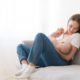 Mother is breastfeeding her kid sitting against light window background. Mom is suckling baby boy at home