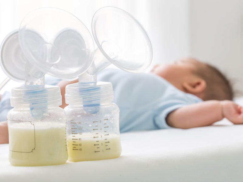 Breast milk pump and baby lying on the white bed. This article answers the question "will not pumping at night decrease my milk supply?"