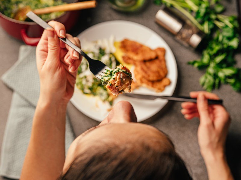 Person sitting at table eating dinner including salmon and salad. This article discusses the best low carb foods that increase milk supply.