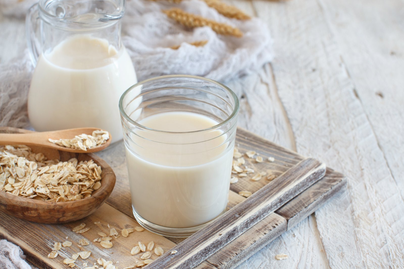 Vegan homemade oat milk in a glass on a wooden tray.