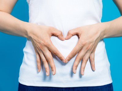 Woman in white shirt making a heart on her gut with her hands. This articles discusses the best probiotics for nursing moms.