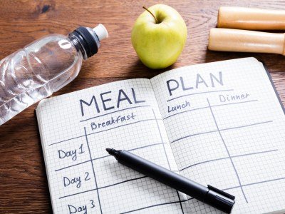 Meal plan journal, pen, bottle or water, and apple on a table. This article reviews breastfeeding meal plan samples.